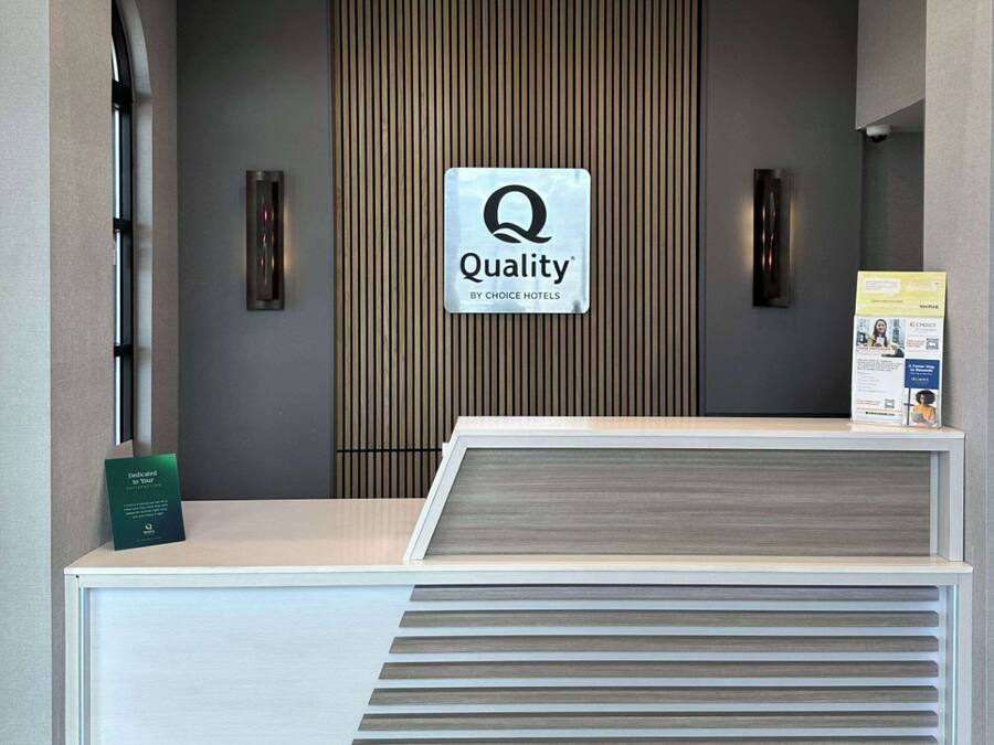 Una recepción con un cartel de 'Quality by Choice Hotels', un panel de madera vertical y una pequeña vitrina informativa.