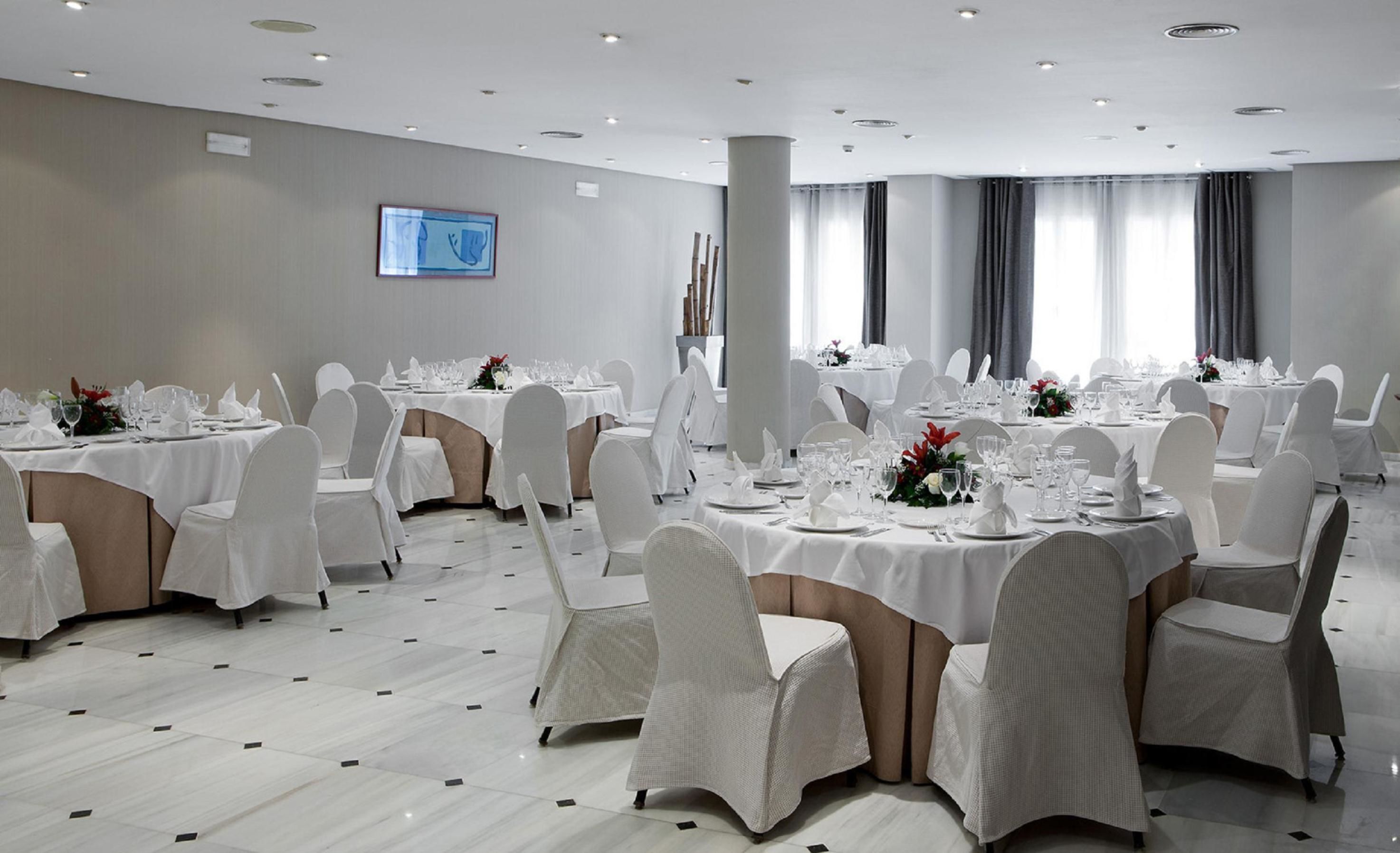 Un salón de banquetes con mesas redondas dispuestas para comer, sillas blancas y un pilar grande.