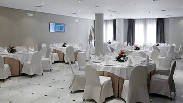 Un salón de banquetes con mesas redondas dispuestas para comer, sillas blancas y un pilar grande.