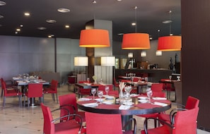 A restaurant with red chairs and tables, large orange pendant lights, and a modern interior design. - URH Ciutat de Mataró (Mataro)