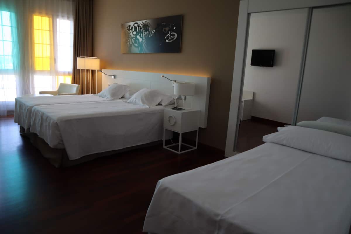 Una habitación de hotel con dos camas, un escritorio, una silla y un cuadro en la pared.