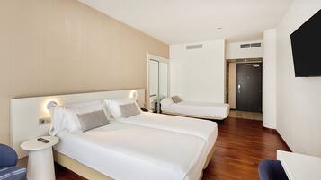 Quarto de hotel com duas camas, uma escrivaninha, uma cadeira, uma televisão e um guarda-roupa.