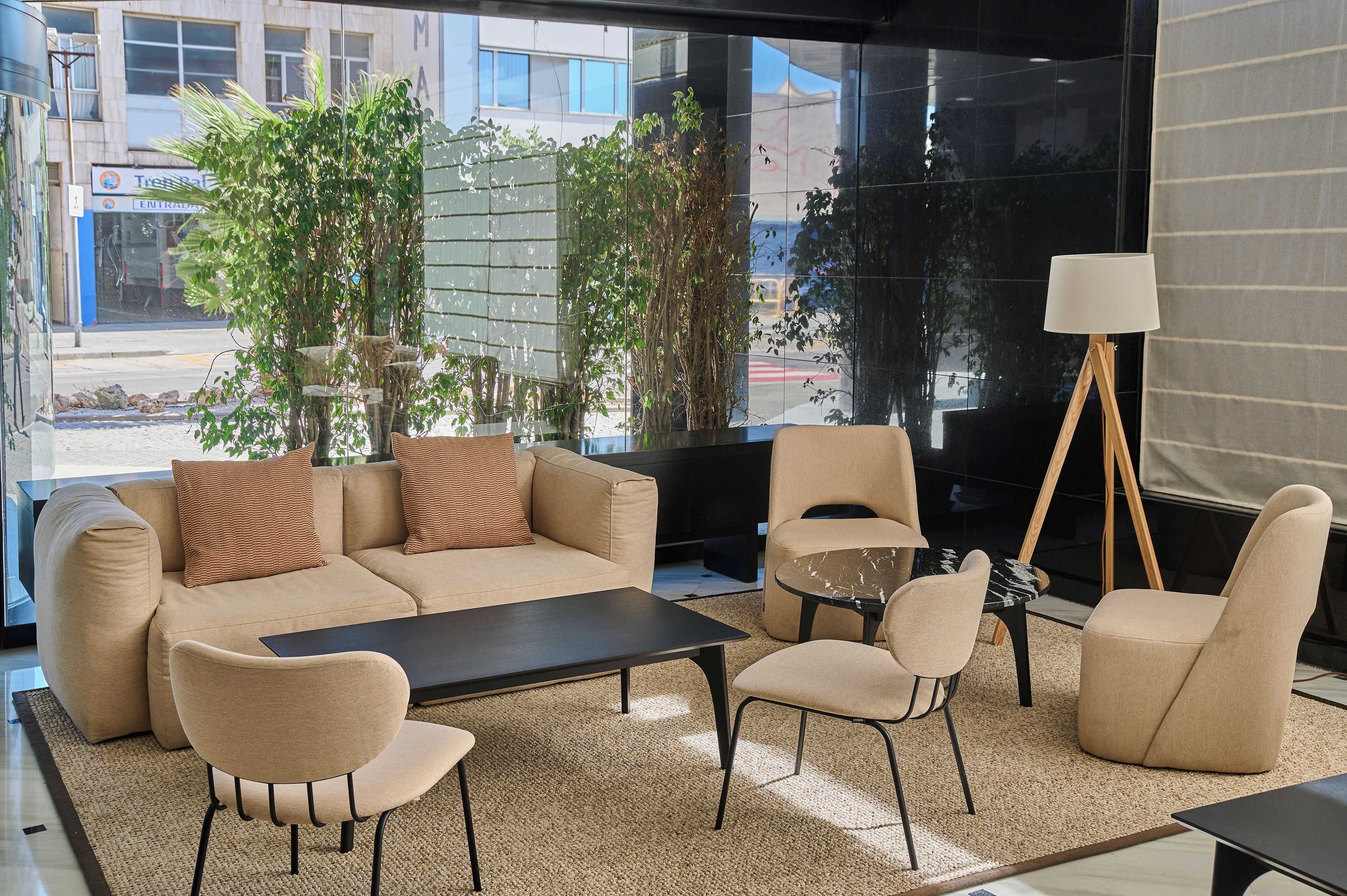 Een moderne woonkamer met een zithoek, een salontafel en stoelen. Er is een groot raam met uitzicht op gebouwen.