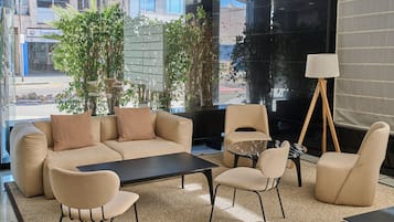 A modern living room with a sofa set, a coffee table, and chairs. There is a large window with a view of buildings outside.