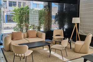 Un salon moderne avec un ensemble de canapés, une table basse et des fauteuils. Une grande fenêtre offre une vue sur les bâtiments environnants.