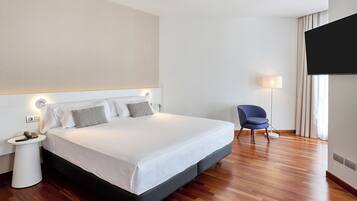Una habitación de hotel con cama, mesita de noche, lámpara, silla y televisor.
