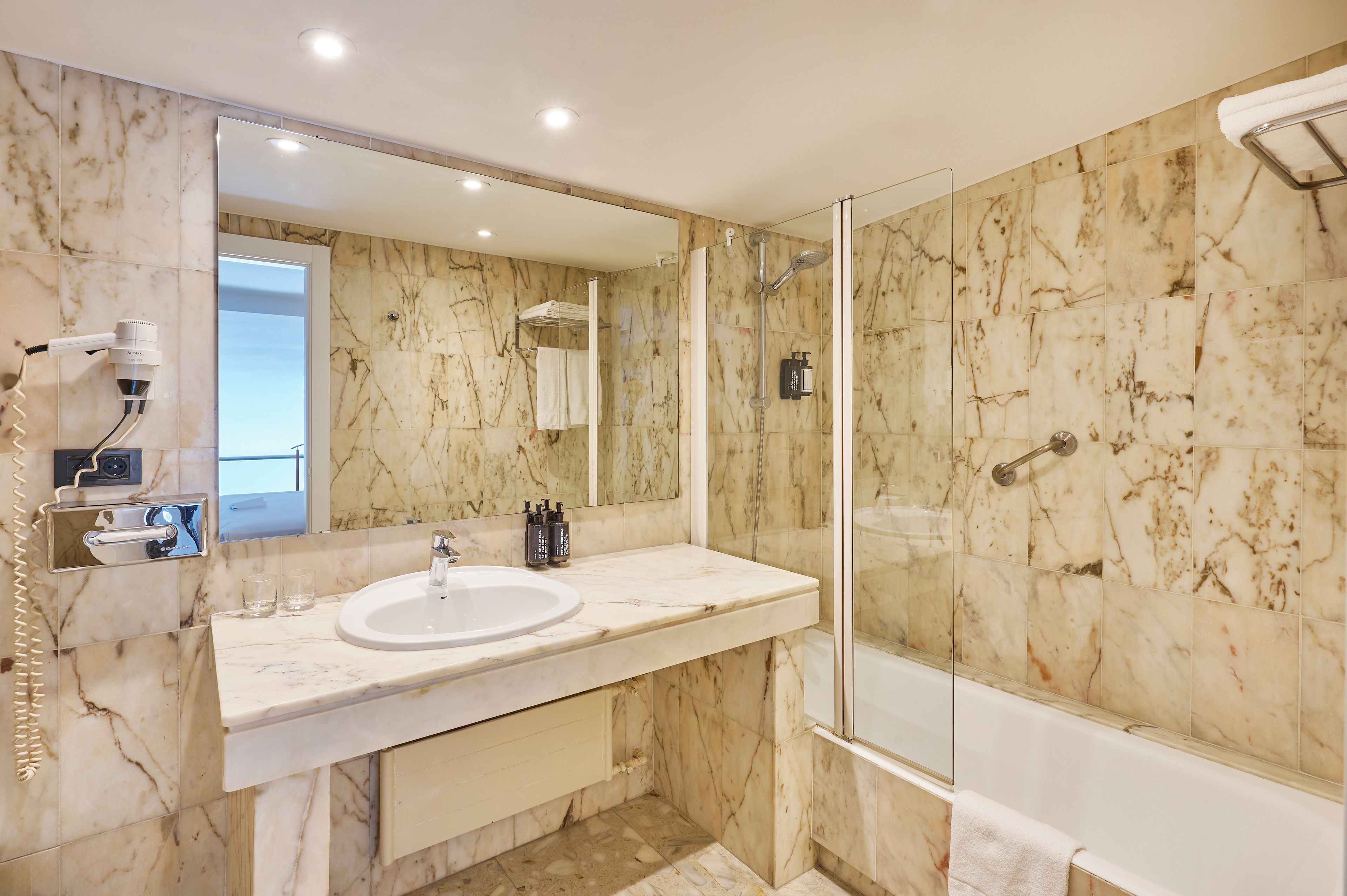 A bathroom with a marble sink, a glass-enclosed shower, and a mirror.