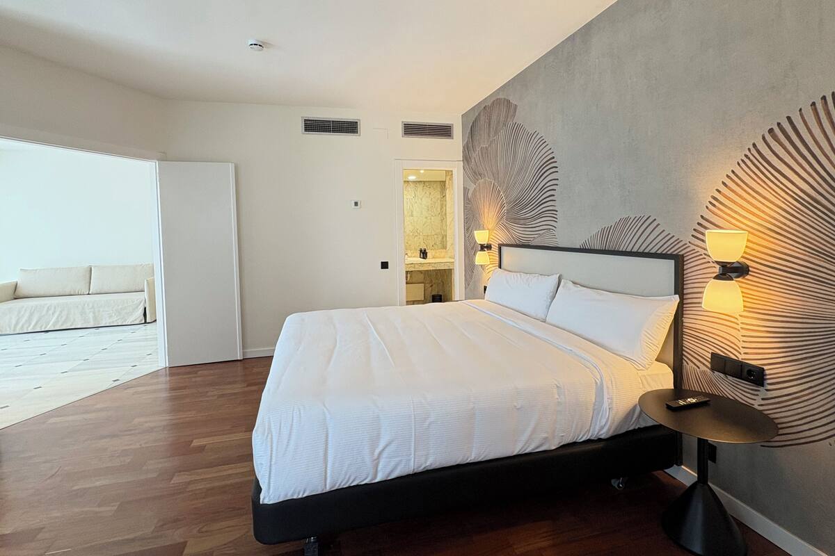 Un dormitorio moderno con una cama grande, lámparas de noche, un espejo y vistas a un balcón.