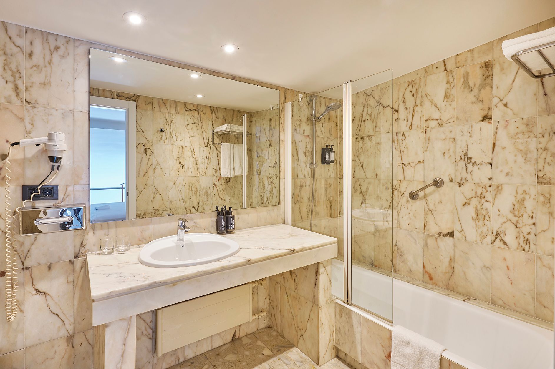Un baño moderno con tocador de mármol, un espejo grande, ducha con cerramiento de vidrio y secador de pelo de mano.