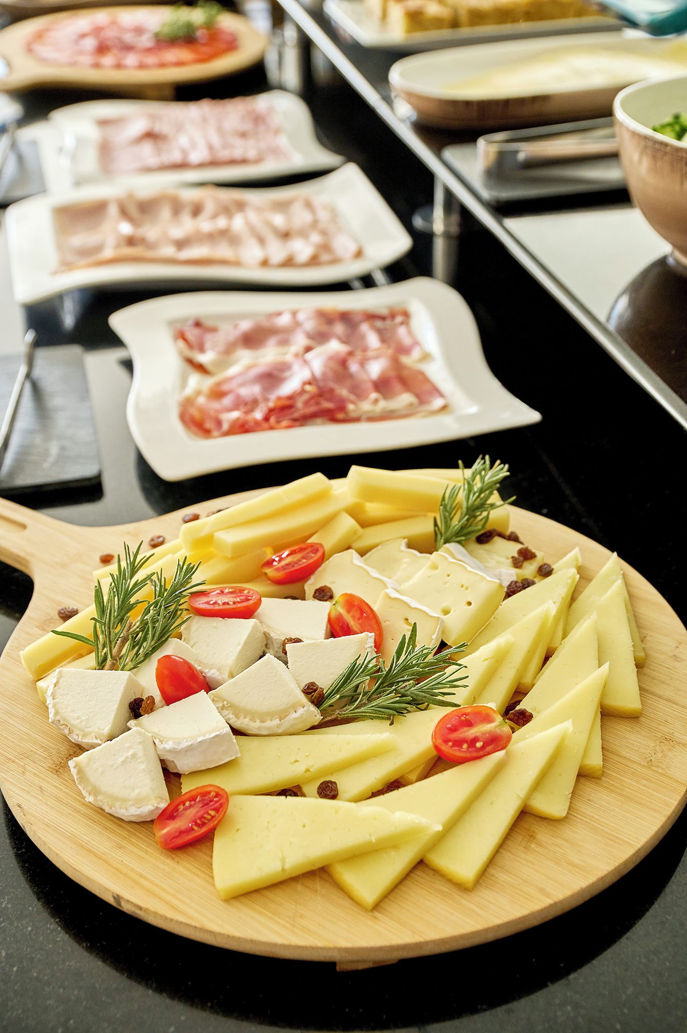 A cheese board with various cheeses, tomatoes, and rosemary.
