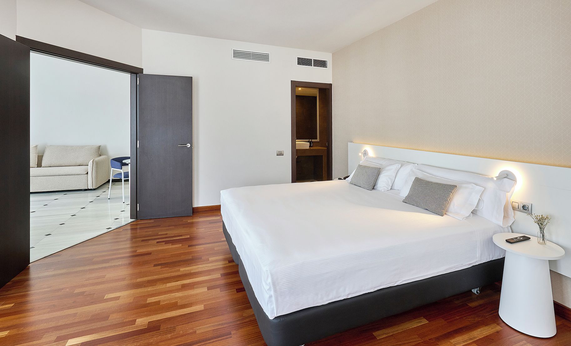 A modern hotel room with a large bed, a bedside table with a lamp, and a view of a balcony.