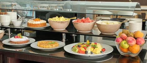 A buffet with various dishes including fruit, desserts, and a cake.