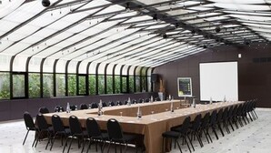 Ein Konferenzraum mit einem langen Tisch, Stühlen, einer Projektionsleinwand und großen Fenstern.