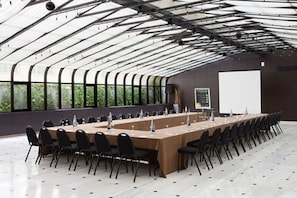 Une salle de conférence équipée d’une longue table, de chaises, d’un écran de projection et de grandes fenêtres.