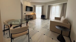 Une chambre d’hôtel moderne avec une table à manger en verre, un canapé, une télévision et un bureau avec une chaise.