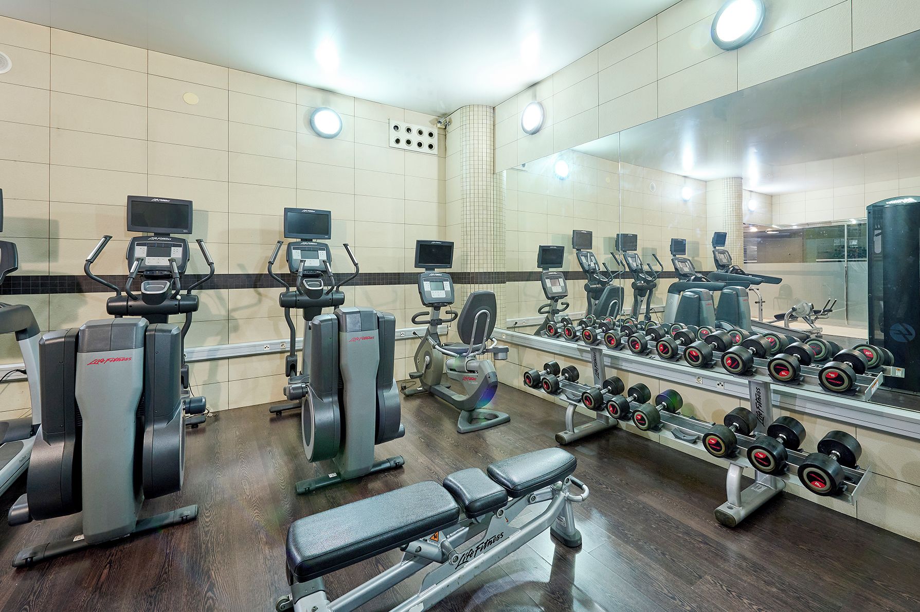 A gym with various exercise equipment, including treadmills, ellipticals, and a bench.