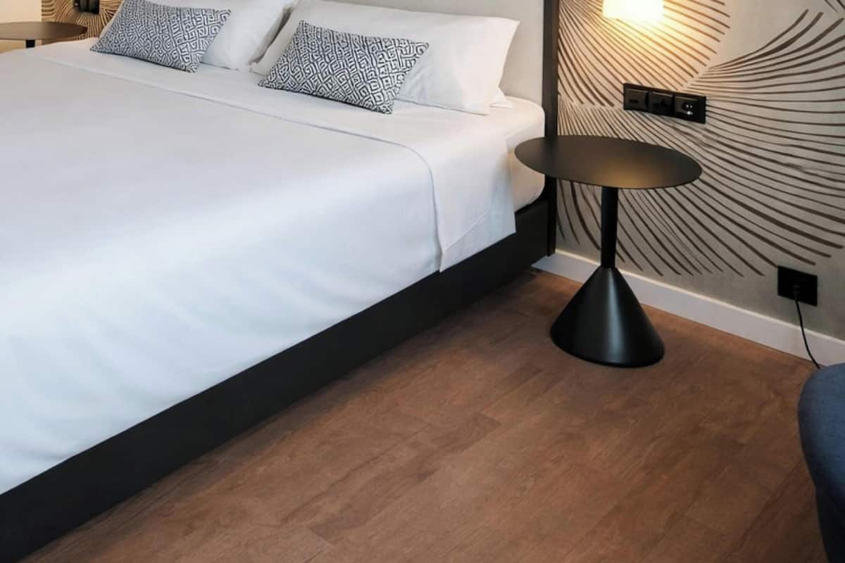Habitación de hotel moderna con una cama grande, una mesita redonda, una lámpara de pared y un papel tapiz estampado.