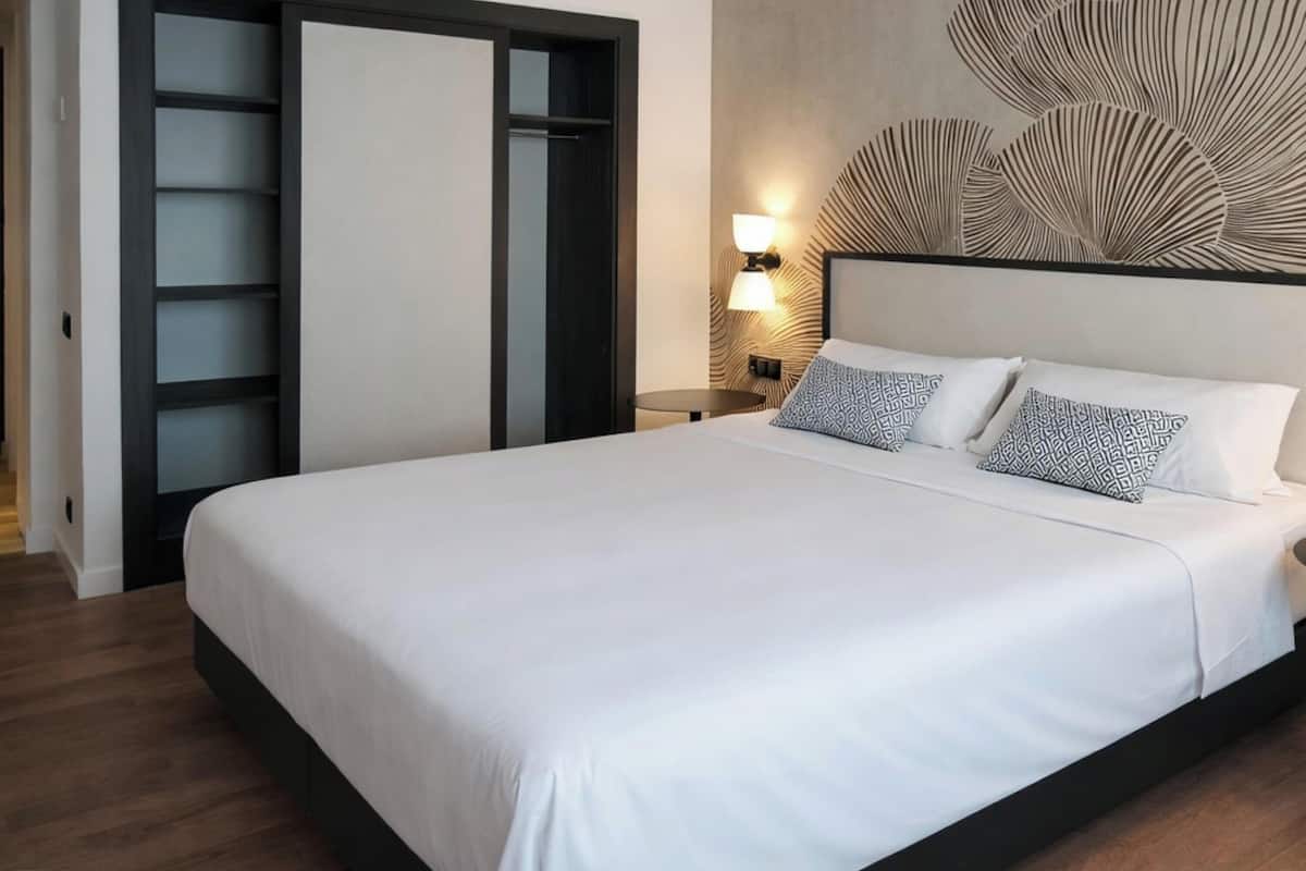 Una habitación de hotel moderna con una cama grande, un armario con puertas correderas, una lámpara fijada a la pared y un panel decorativo.