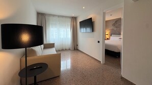 Une chambre d’hôtel équipée d’un canapé, d’un téléviseur fixé au mur, d’un lit avec une tête de lit et d’une petite table avec une télécommande.