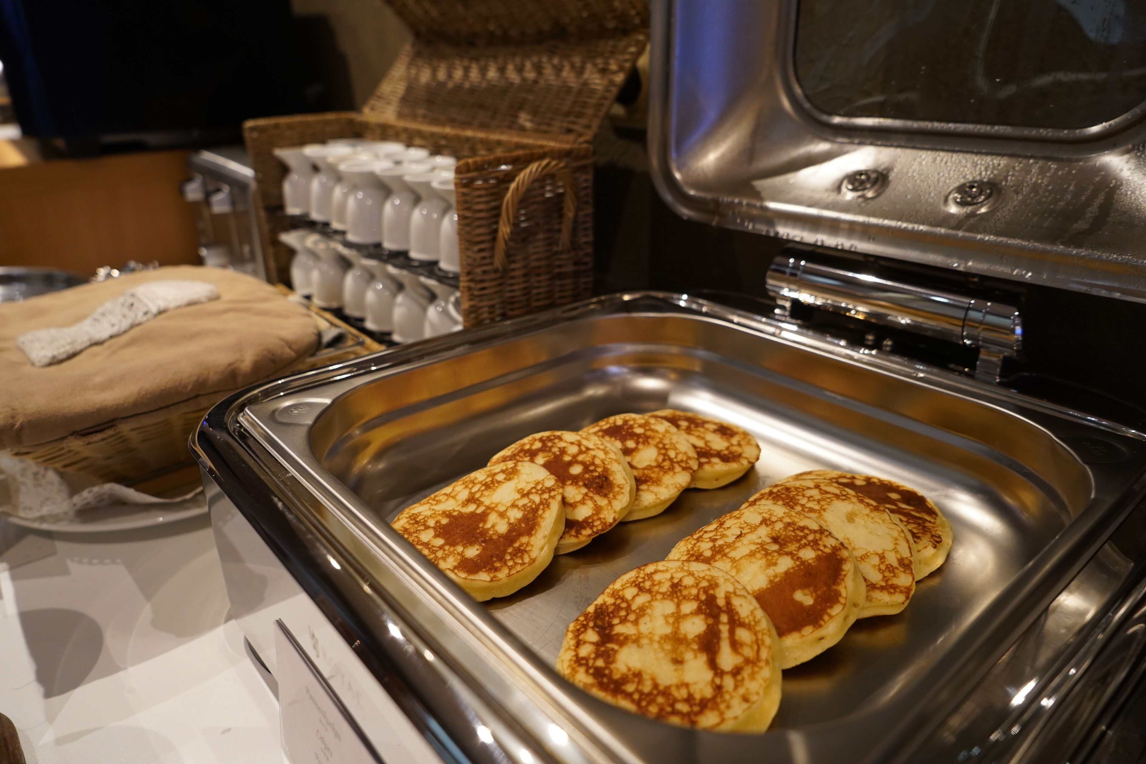 A buffet table with a tray of pancakes and a basket of eggs.