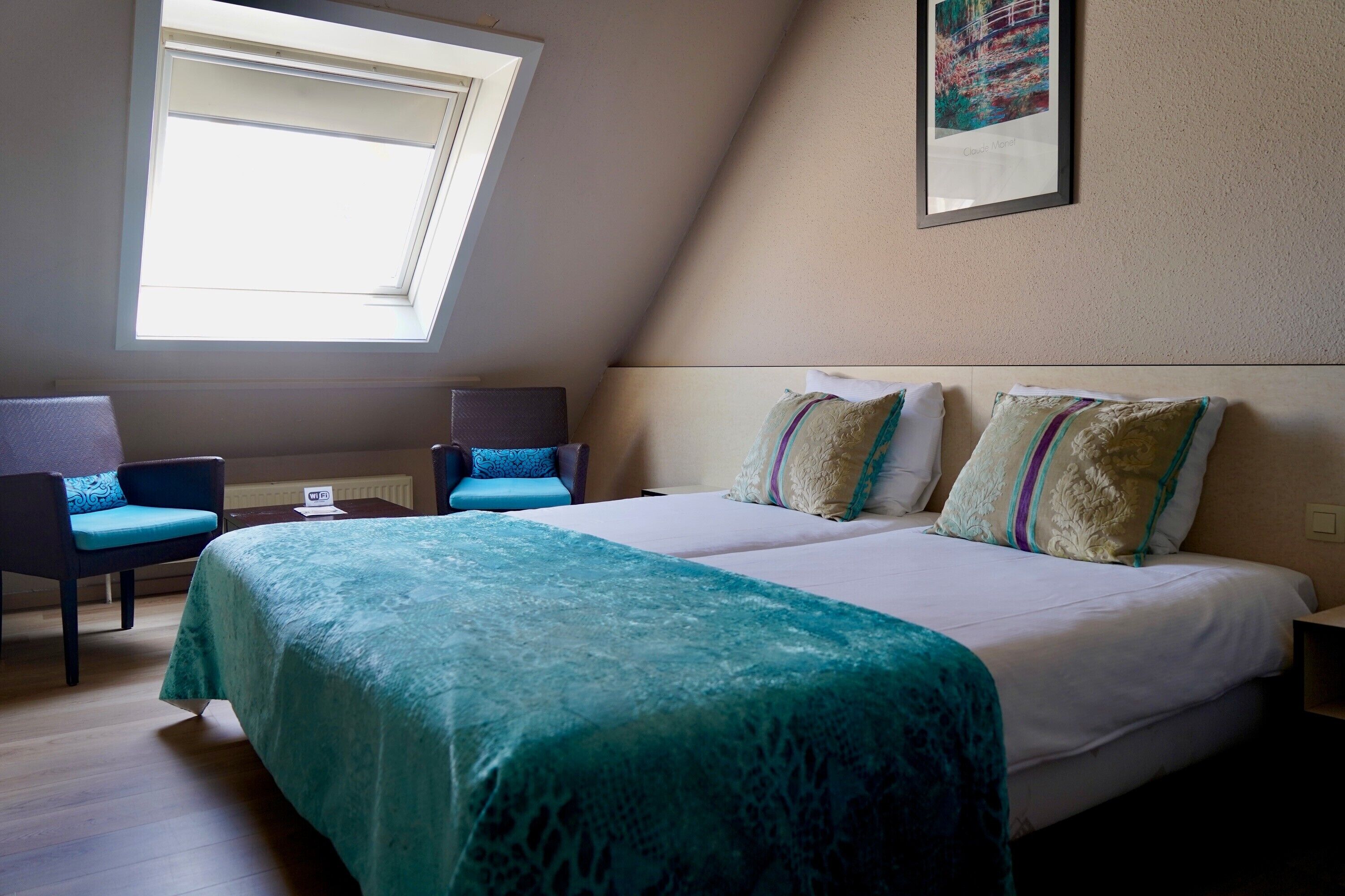 A bedroom with a large bed, two chairs, a window, and a framed picture on the wall.