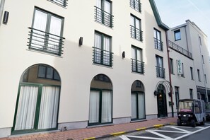 A hotel facade with multiple windows, a prominent entrance, and a small vehicle parked in front.