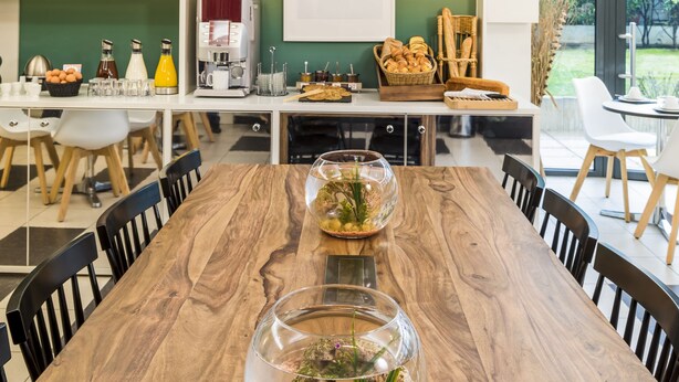 Eine moderne Küche mit Esstisch aus Holz, Korbschwinglampen und einer Kücheninsel mit Geräten und einer Kaffeestation.
