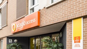 Ein Gebäude mit einem Schild, das „Adagio Access“ zeigt, und einem großen Topfpflanzen vor der Fassade.