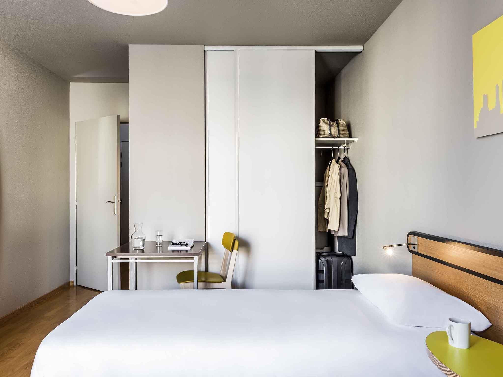 A hotel room with a bed, a desk with a chair, a wardrobe, and a coat rack.