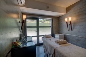 A modern spa room with a massage table, a small sink, and a window with a view of greenery.