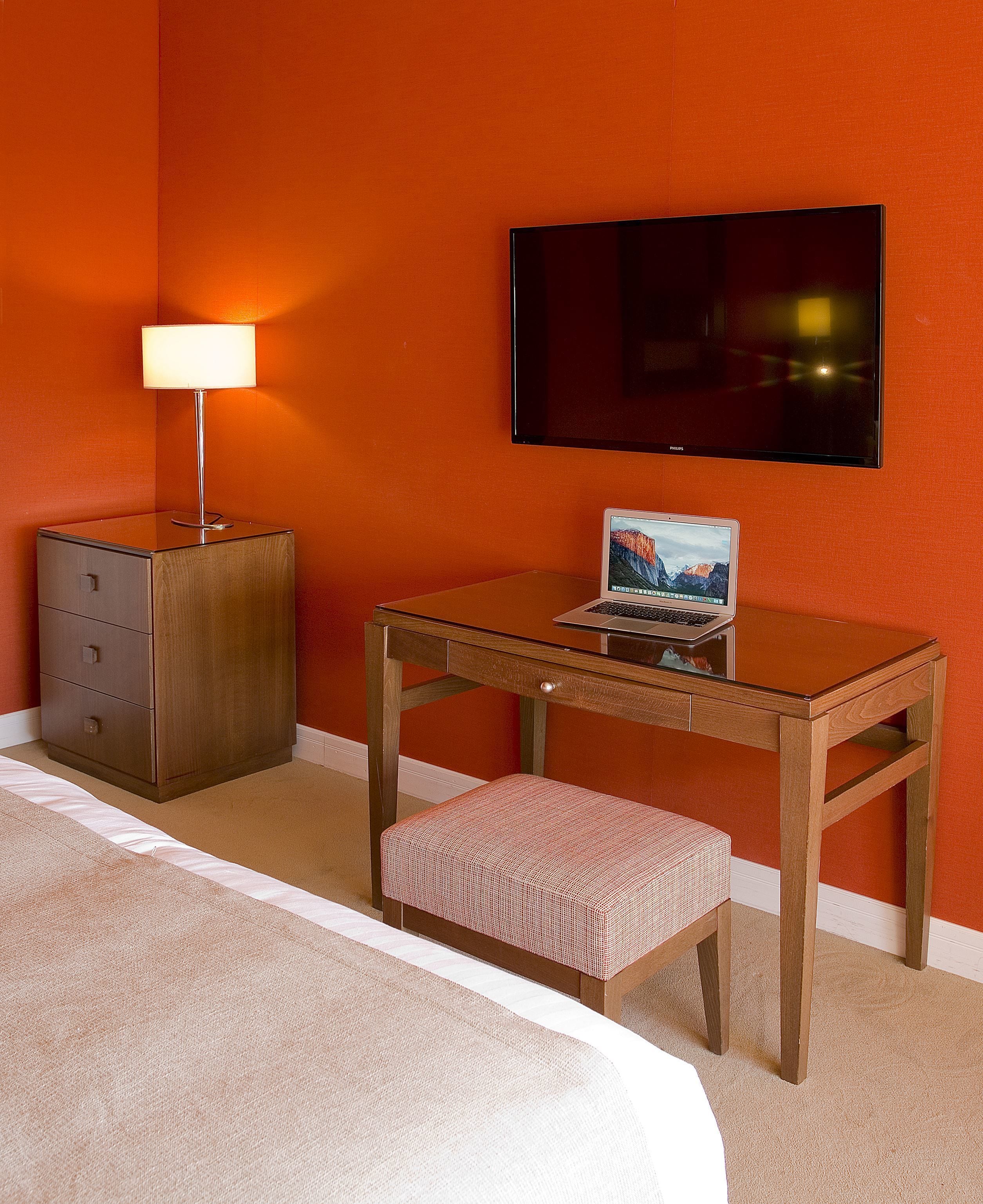 Una habitación de hotel con una cama, un escritorio con una computadora portátil, un televisor y una mesita de noche con una lámpara.
