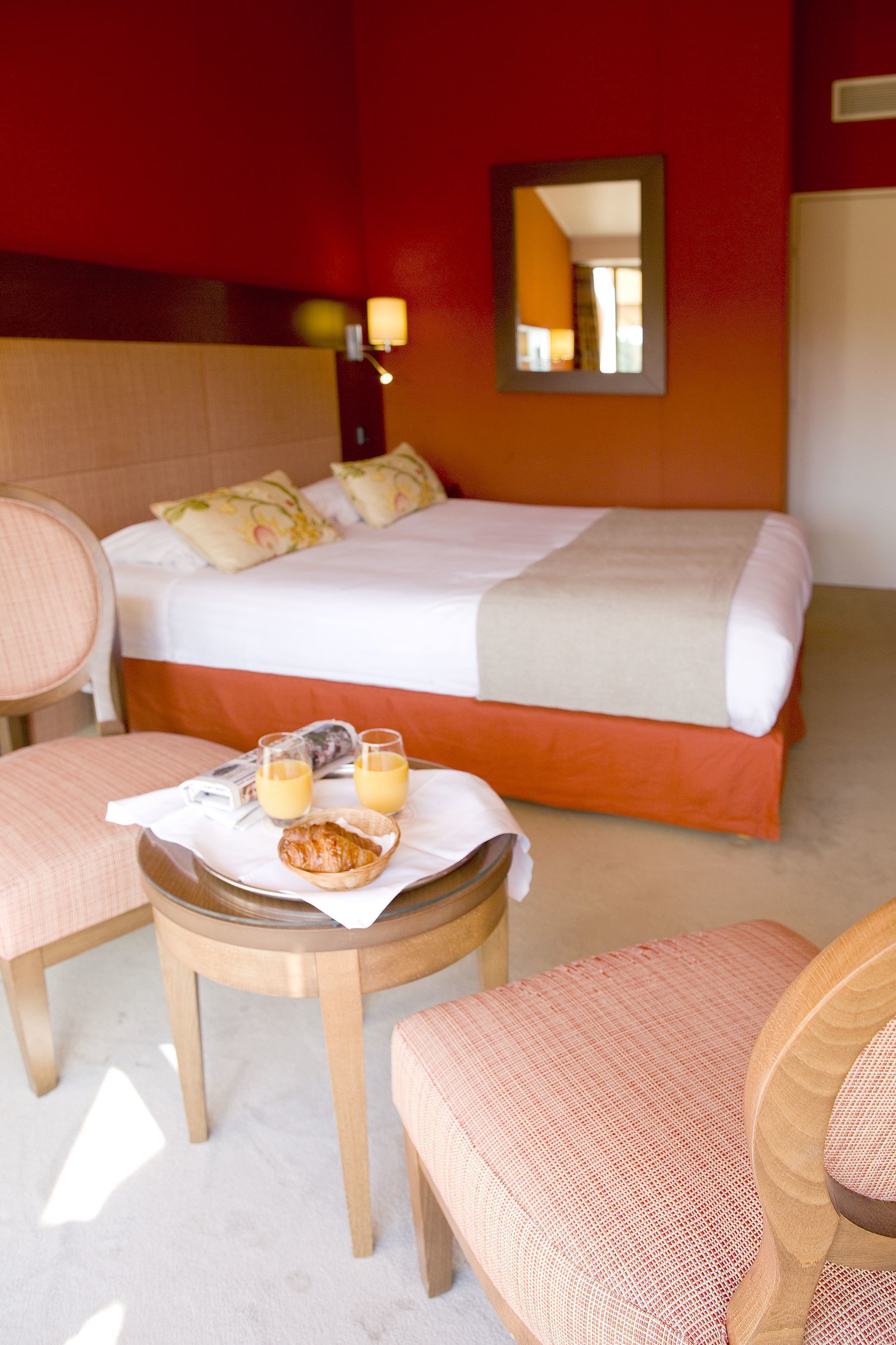 A hotel room with a bed, two chairs, a small table with breakfast items, and a mirror on the wall.