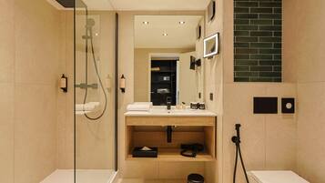 A modern bathroom with a glass-enclosed shower, a wooden vanity, and a black trash bin.