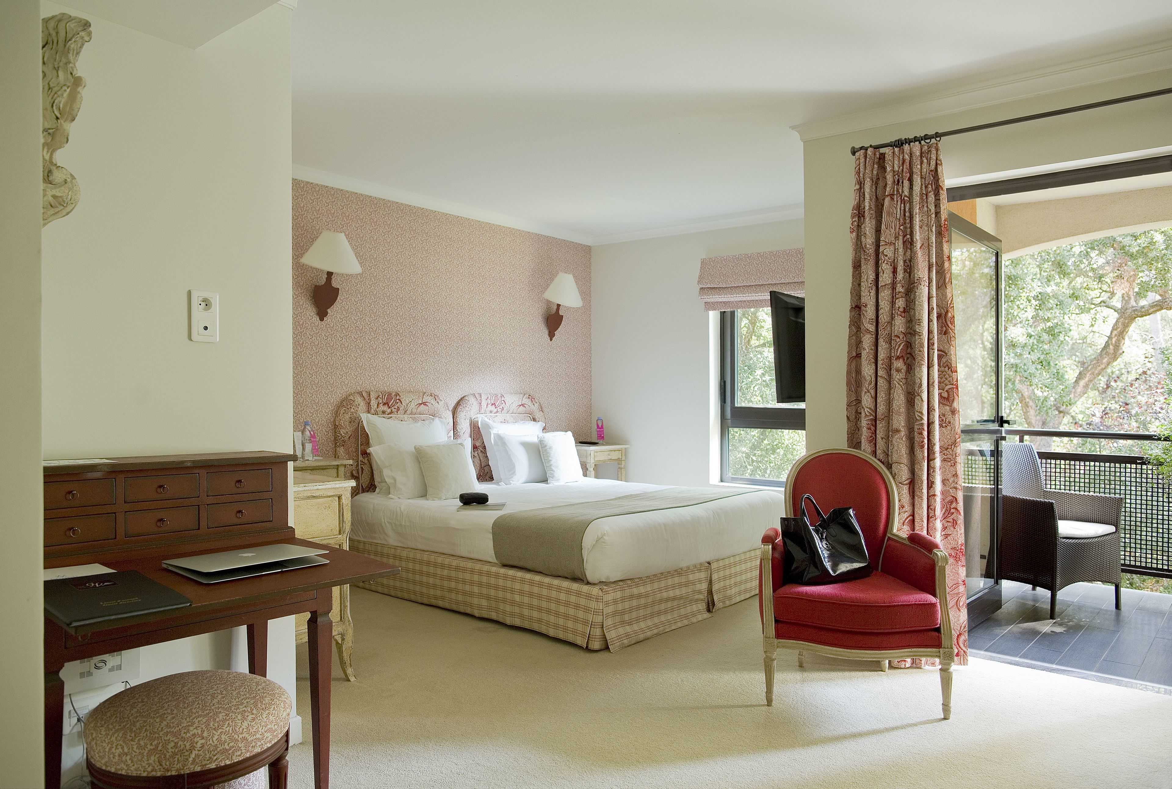 A bedroom with a bed, a desk, a chair, and a balcony with a view.
