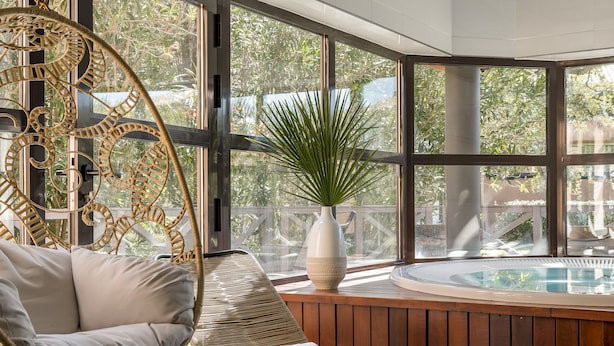 Een kamer met een rieten stoel, een met kussens beklede bank, een potplant en een jacuzzi.