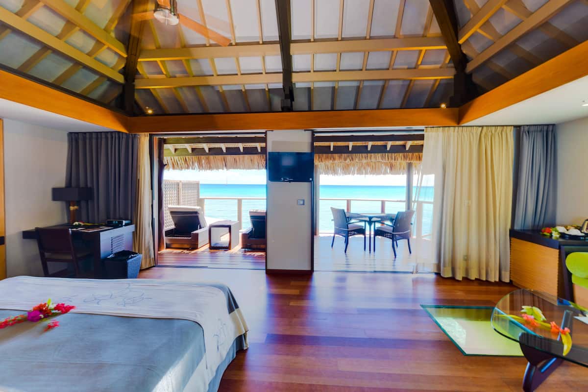 Quarto de hotel com cama, escrivaninha, cadeira, mesa e vista para o oceano.