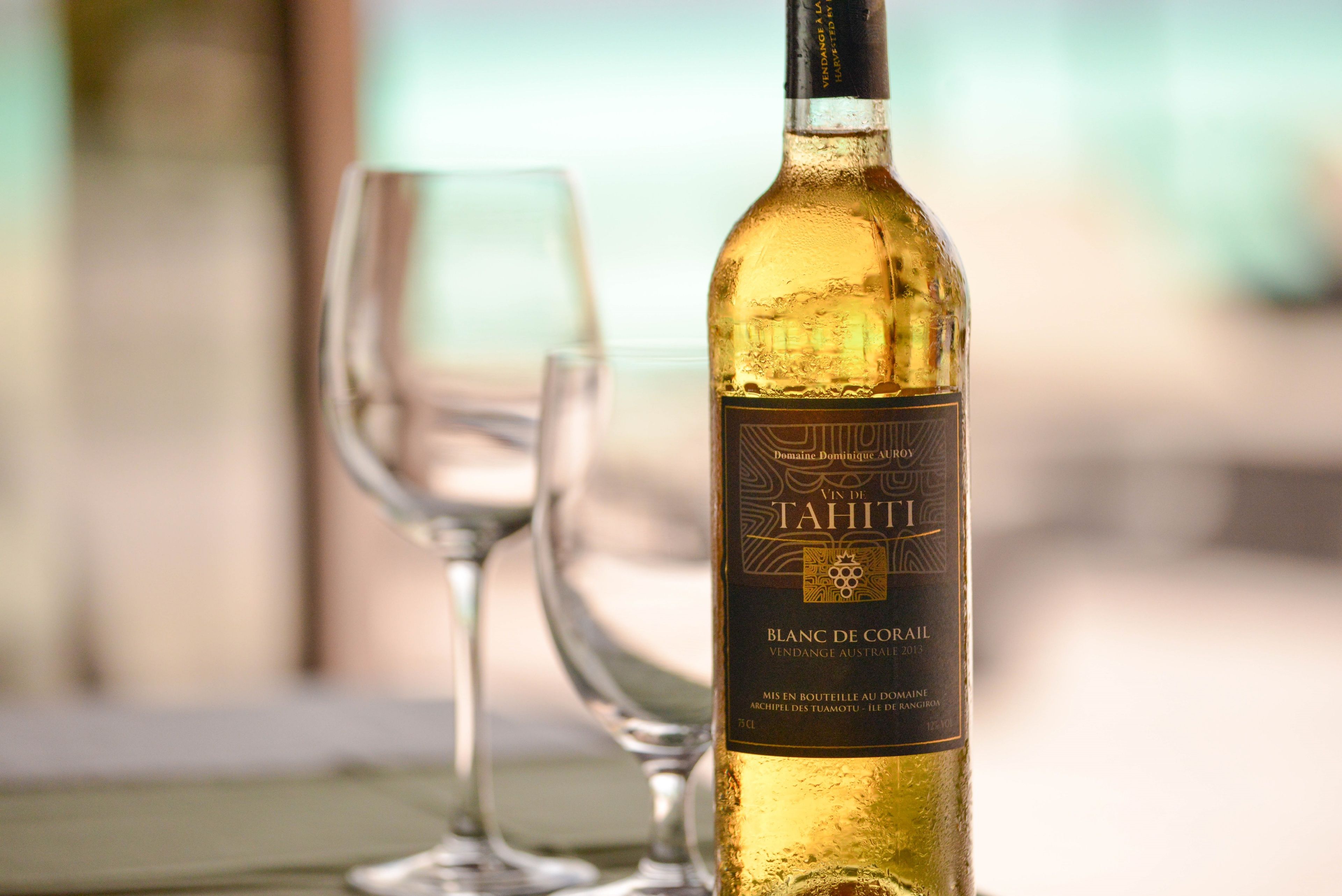 A bottle of Domaine Dominique Auroy Tahiti Blanc De Coraïl wine with a label, placed next to an empty wine glass.