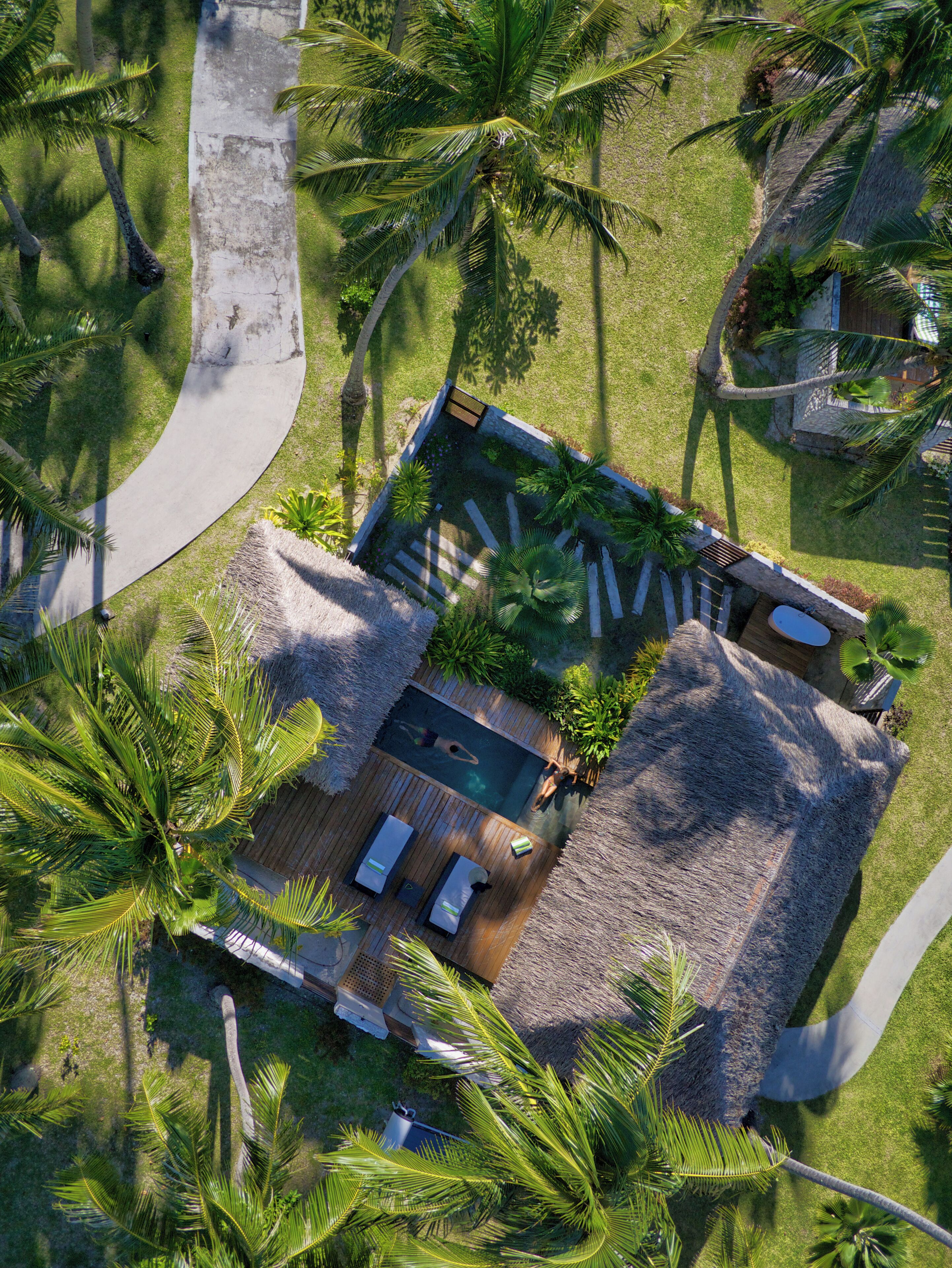 An aerial view of a resort with a swimming pool, lounge area, and tropical vegetation.