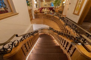 Eine imposante Treppe mit aufwendiger Geländerarbeit und einem polierten Steinboden, die zu einer Sitzgruppe mit einem roten Sofa und einem Tisch führt.