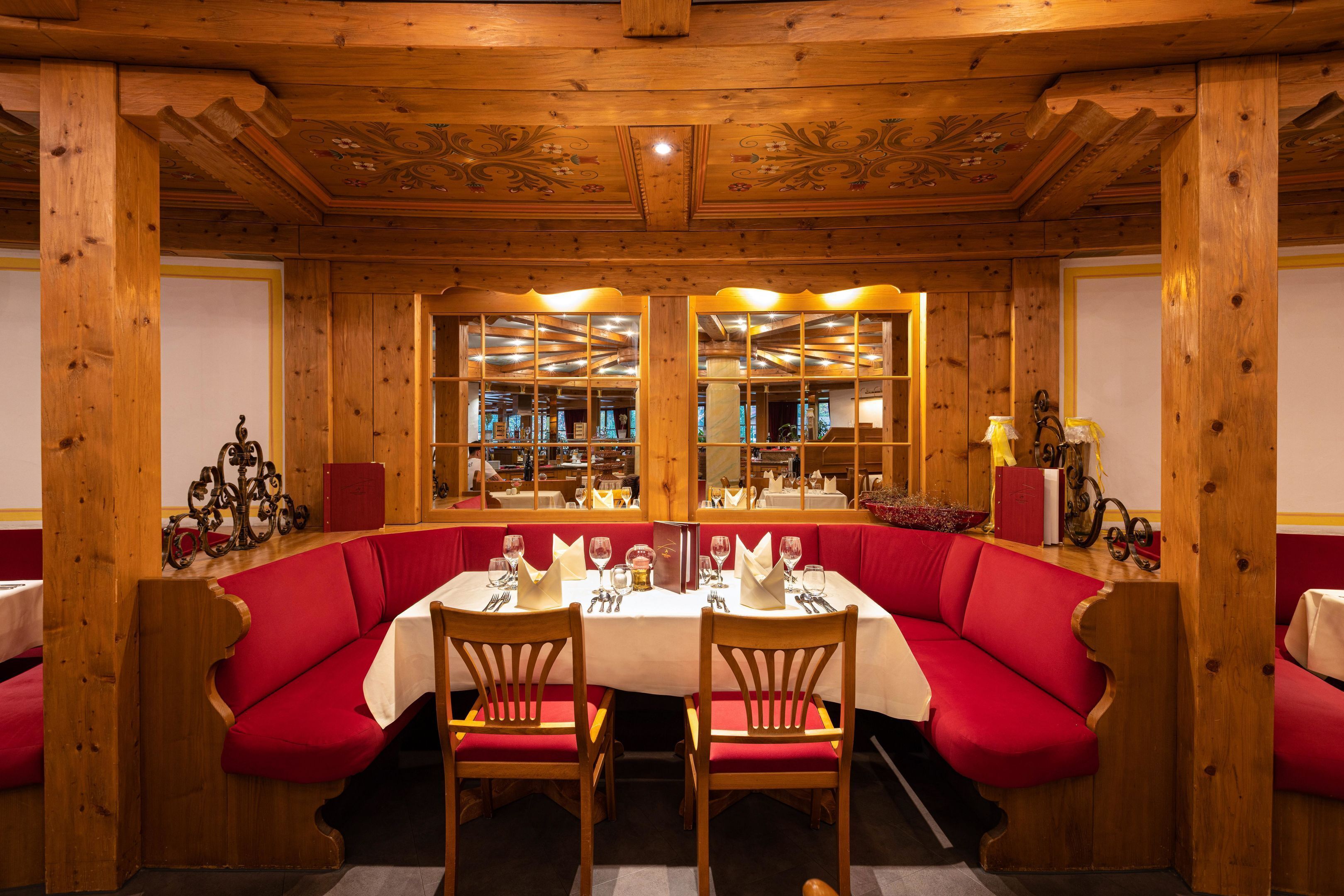 A dining area with a wooden ceiling, red upholstered booths, and a central table set for dining.