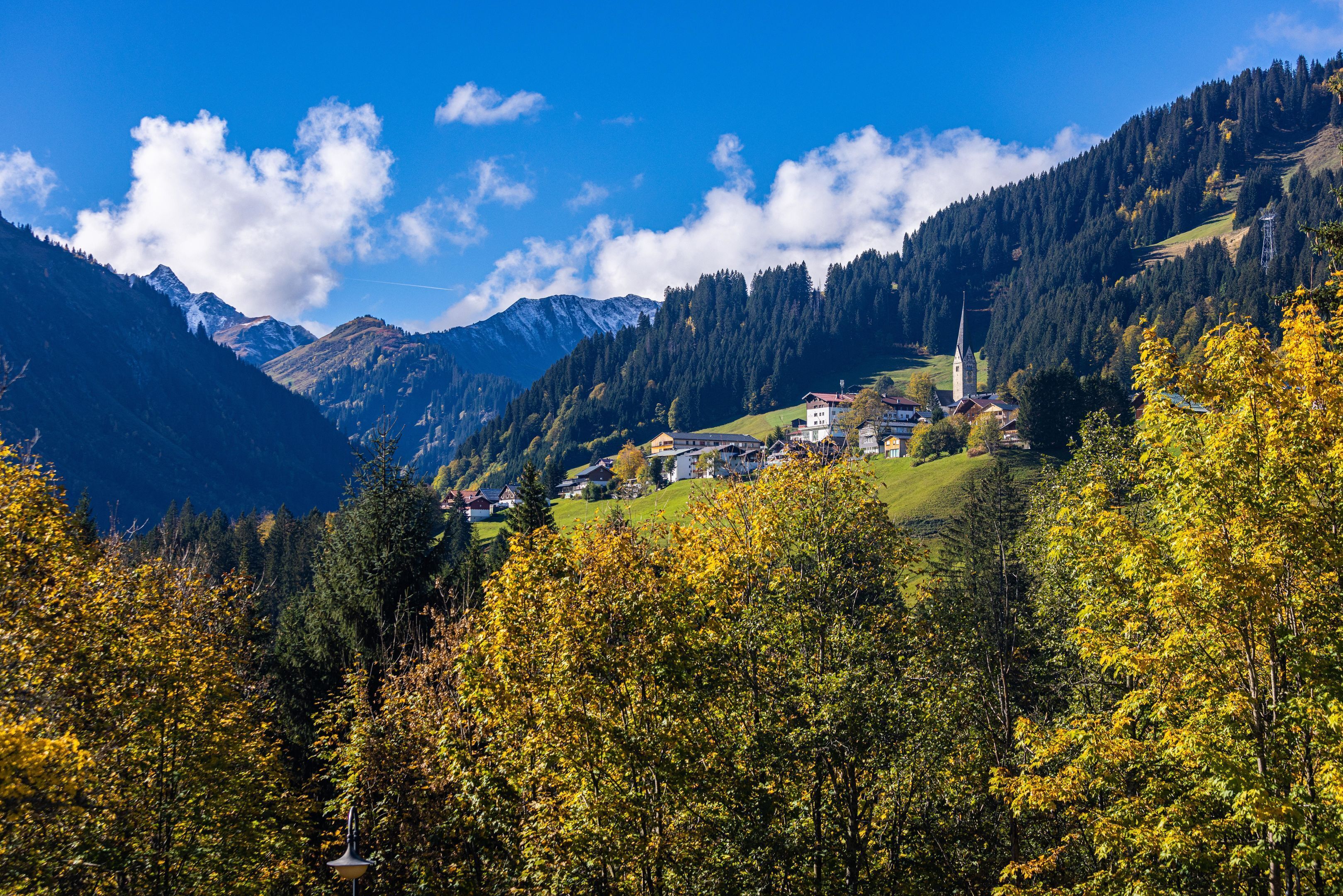 Eine gebirgige Landschaft mit einem Dorf, einer Kirche und Herbstlaub.