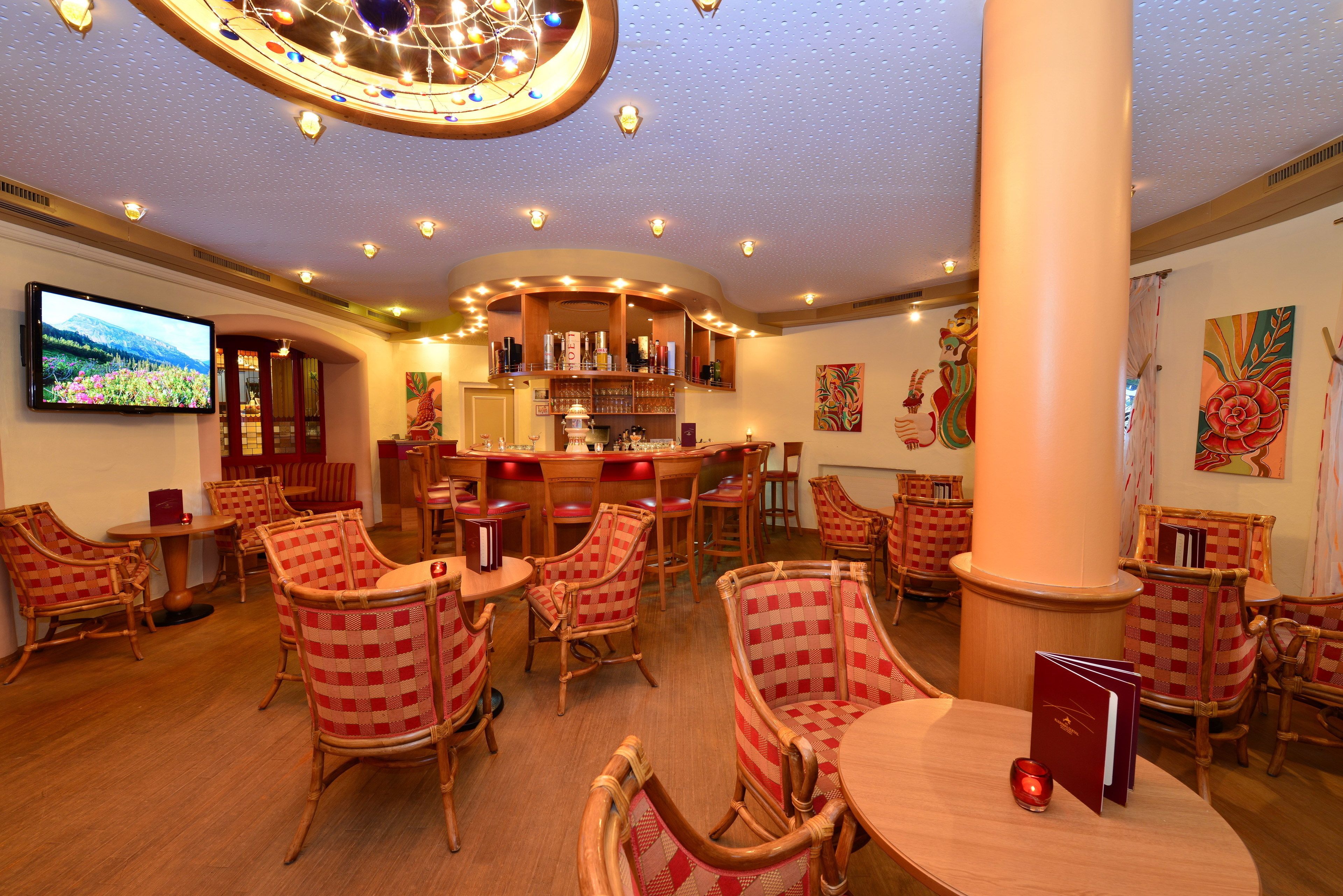 A restaurant with checkered chairs, a bar area, and a television on the wall.