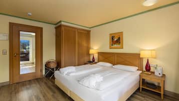 A hotel room with a large bed, two bedside tables, a wooden wardrobe, a door leading outside, and a small basket.