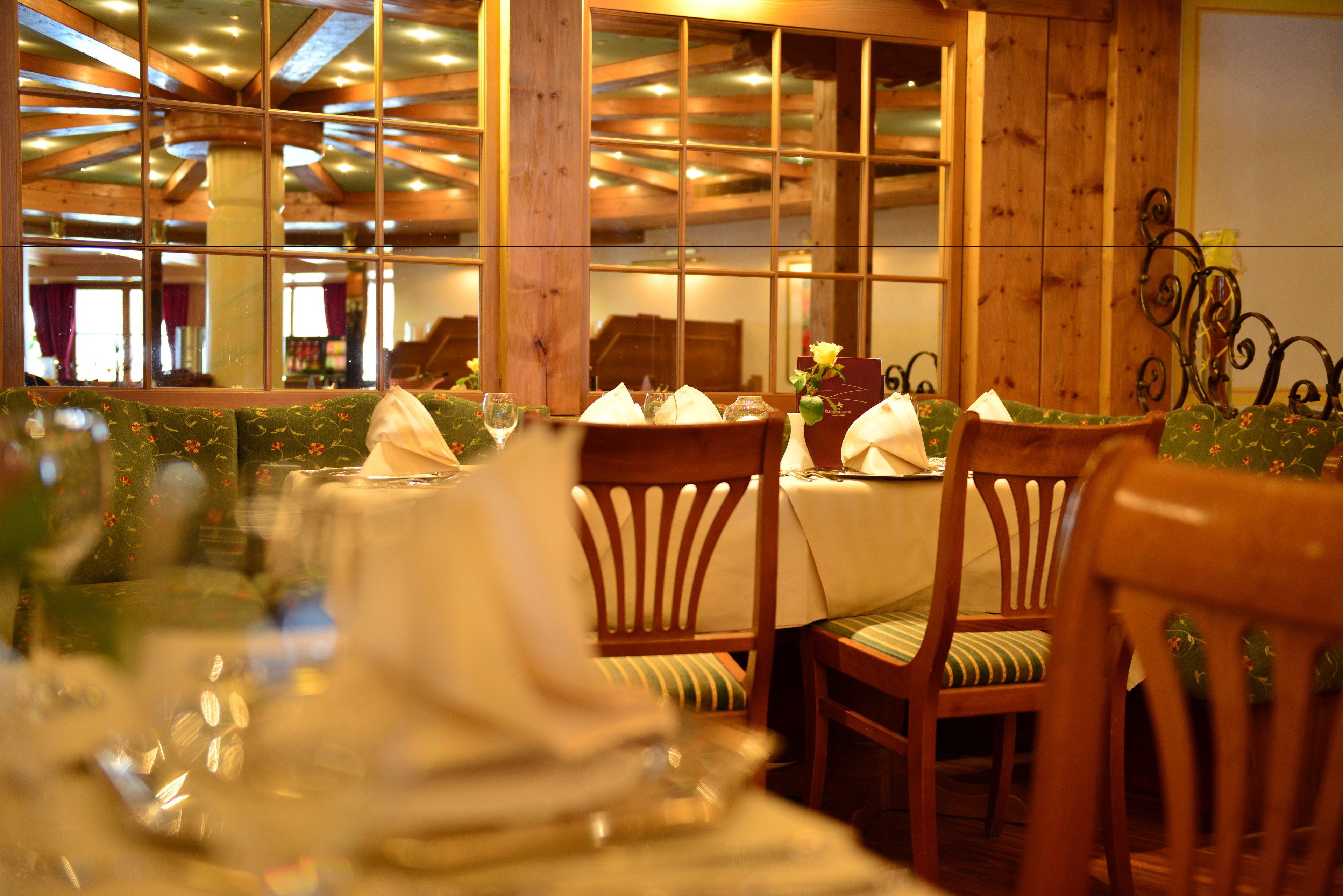 Un comedor con sillas y mesas de madera, ventanas amplias e iluminación cálida en el interior.