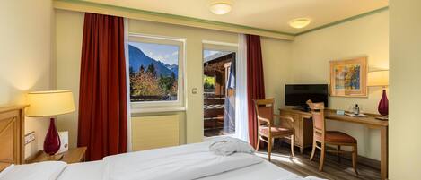 Habitación de hotel con cama, escritorio, silla, televisor y vista a las montañas.