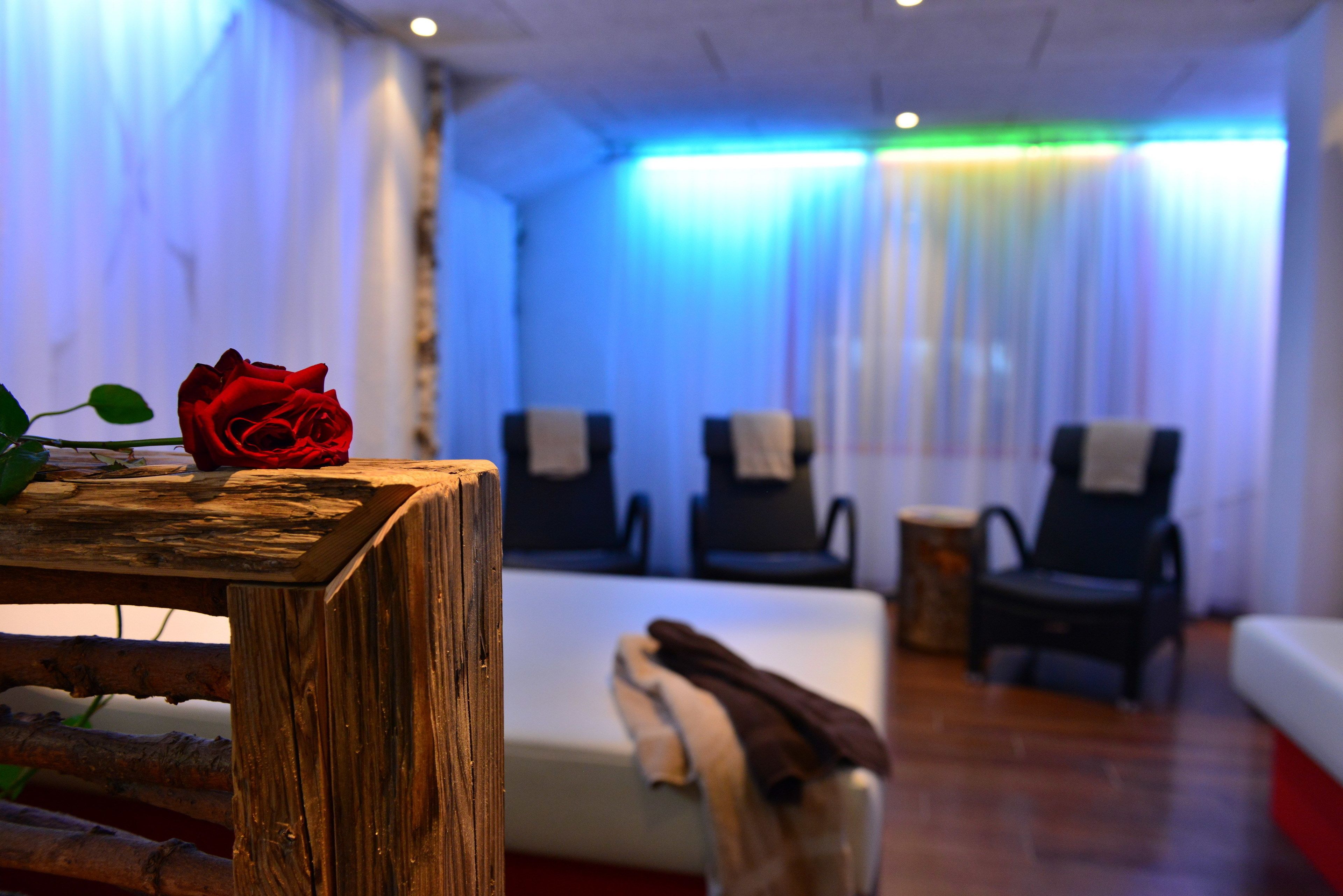 A room with a wooden table, a red rose, two chairs, a bed, and a small table with a towel.