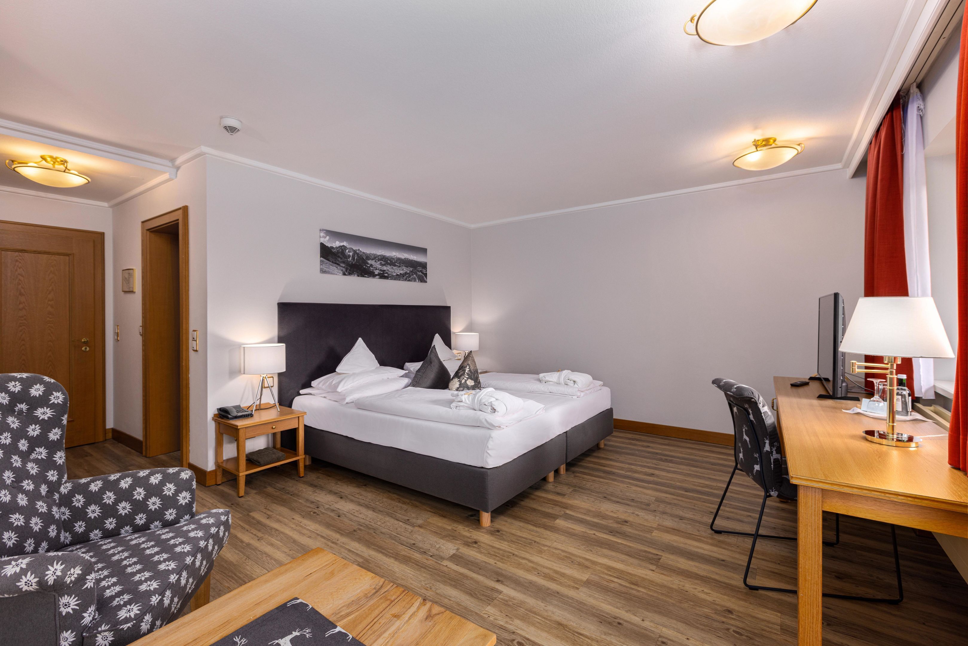 A hotel room with a bed, a chair, a desk, and a television.
