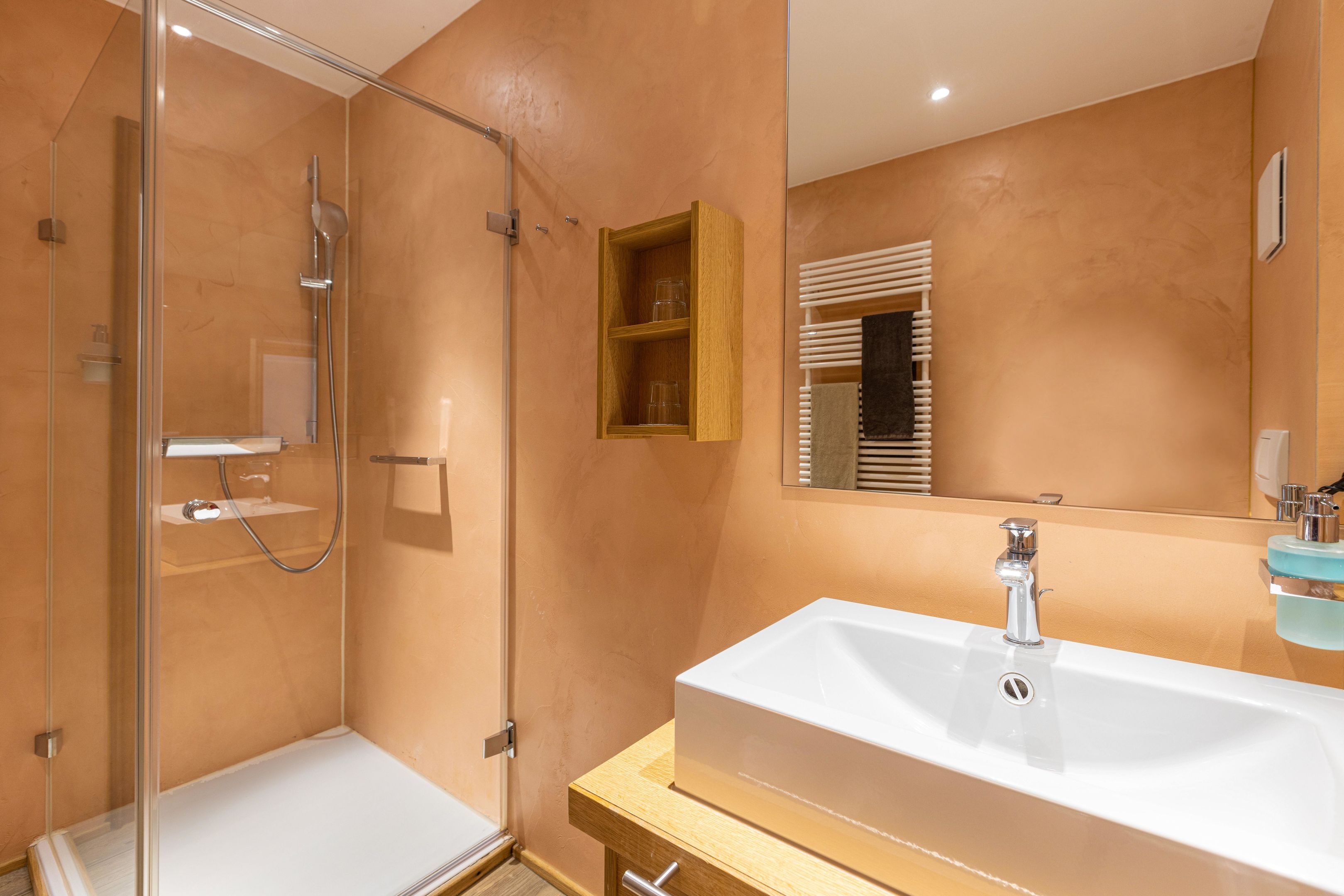 A bathroom with a glass-enclosed shower, a white sink, and a wooden cabinet.