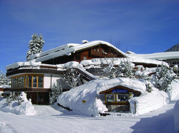 A snow-covered building with a ski lift, a sign indicating it's a wellness hotel, and a mountain backdrop.