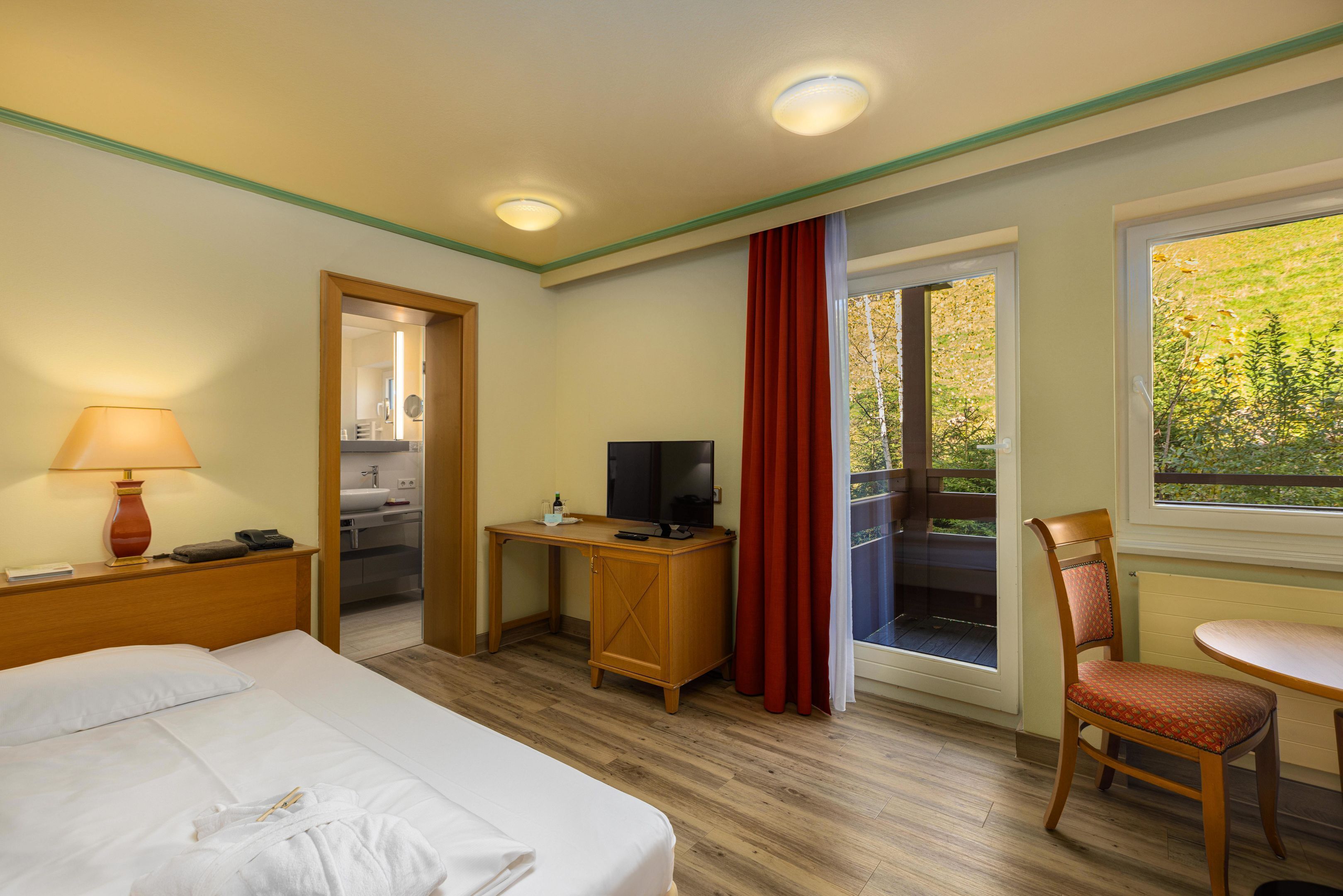A hotel room with a bed, desk, chair, TV, and a view of the outdoors.